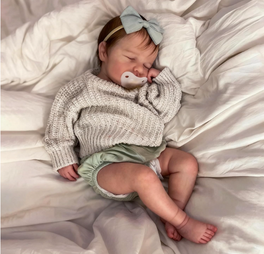 Baby wearing a knitted sweater and green diaper with a bow, lying on a soft surface.